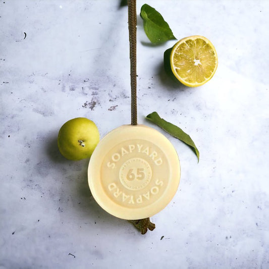 this is a picture of a bergamot soap on a rope on a concrete background with half limes. The article is an Ankorstore vs Faire comparison