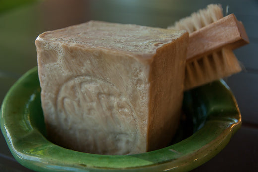 a cube of aleppo soap with arabic writing and a nail brush in a green pottery ashtray type dish