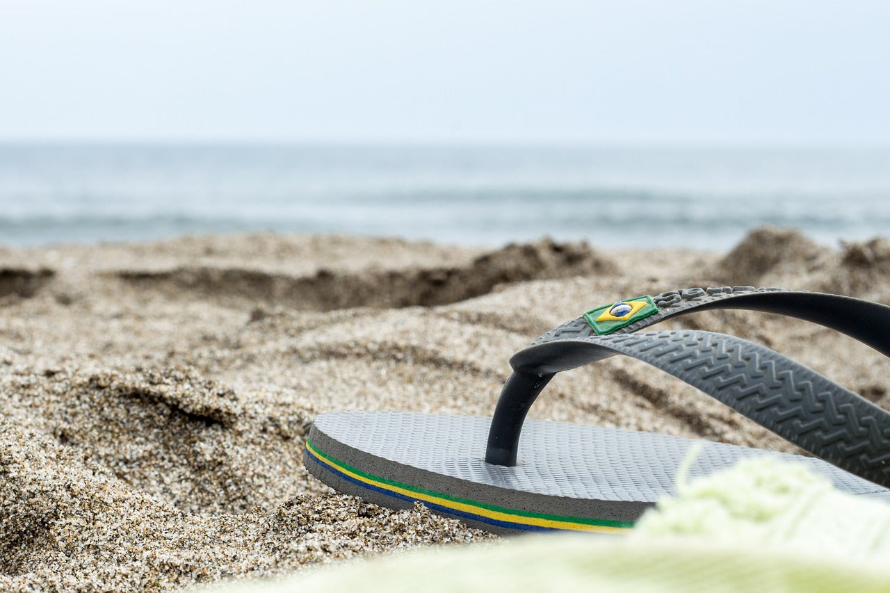 a pair  of flip flops on a beach, symbolic of the article which is about recycling flip flops. only the front half is visible not the whole flip flop