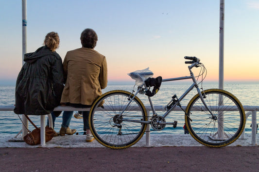 two people sitting looking at the sea next to a bike