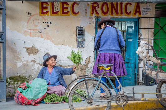 peruvian ladies in tradtional dress outside a run down building with the word painted on a wall and a bike outside