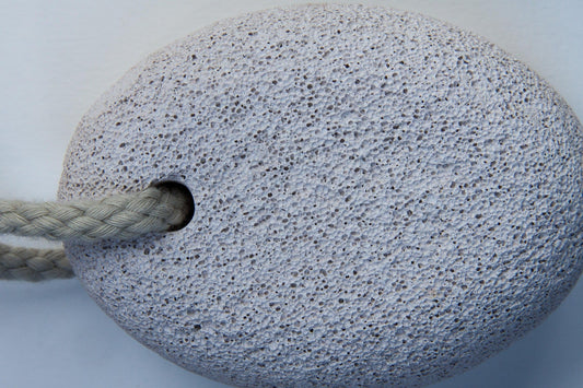 Close-up of a round pumice stone with a braided rope threaded through a hole, showing its porous texture. Ideal for natural exfoliation and skincare.