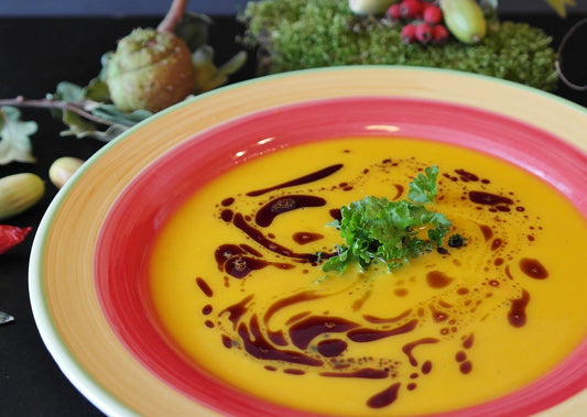 a bowl of yellow soup on a colourful plate