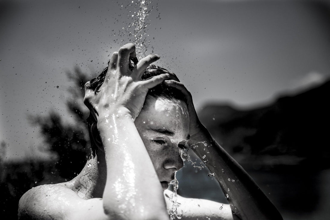 black and white photo a persons head and arms under a shower outdoors